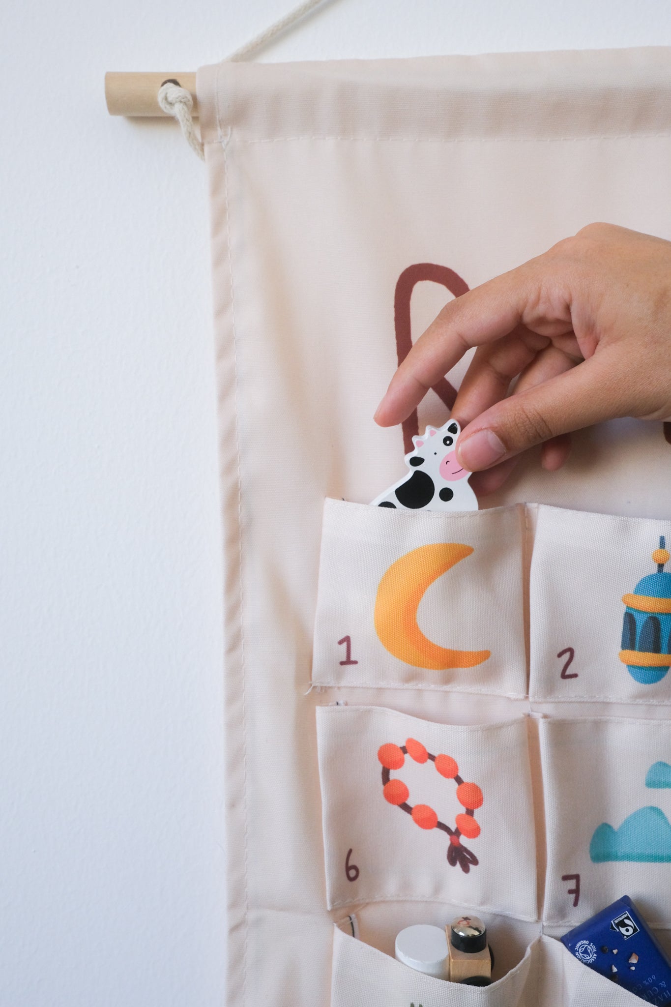 Hand reaching for a pocket on a fabric ramadan calendar with various illustrations.